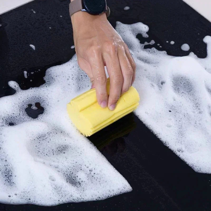 Hand using a yellow sponge to scrub a soapy surface

