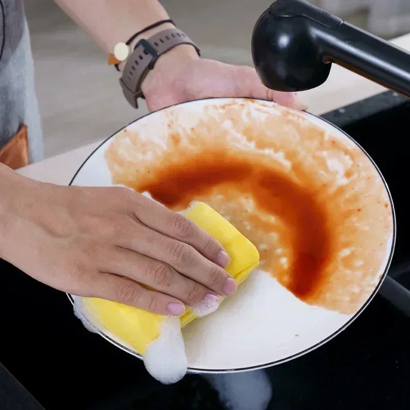 Person cleaning a dish with a sponge, showing food residue.

