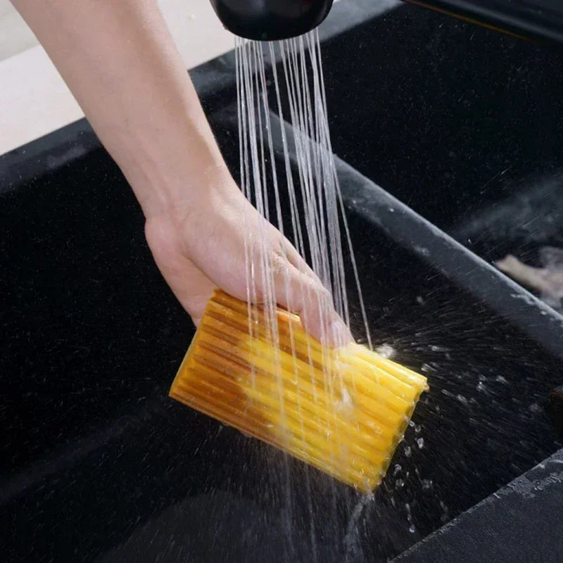 Hand washing a yellow sponge under running water in a sink.

