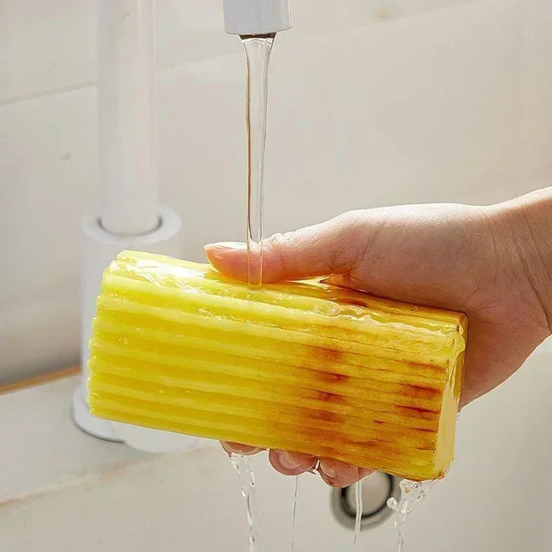 Hand holding a yellow sponge under running water in a bathroom setting

